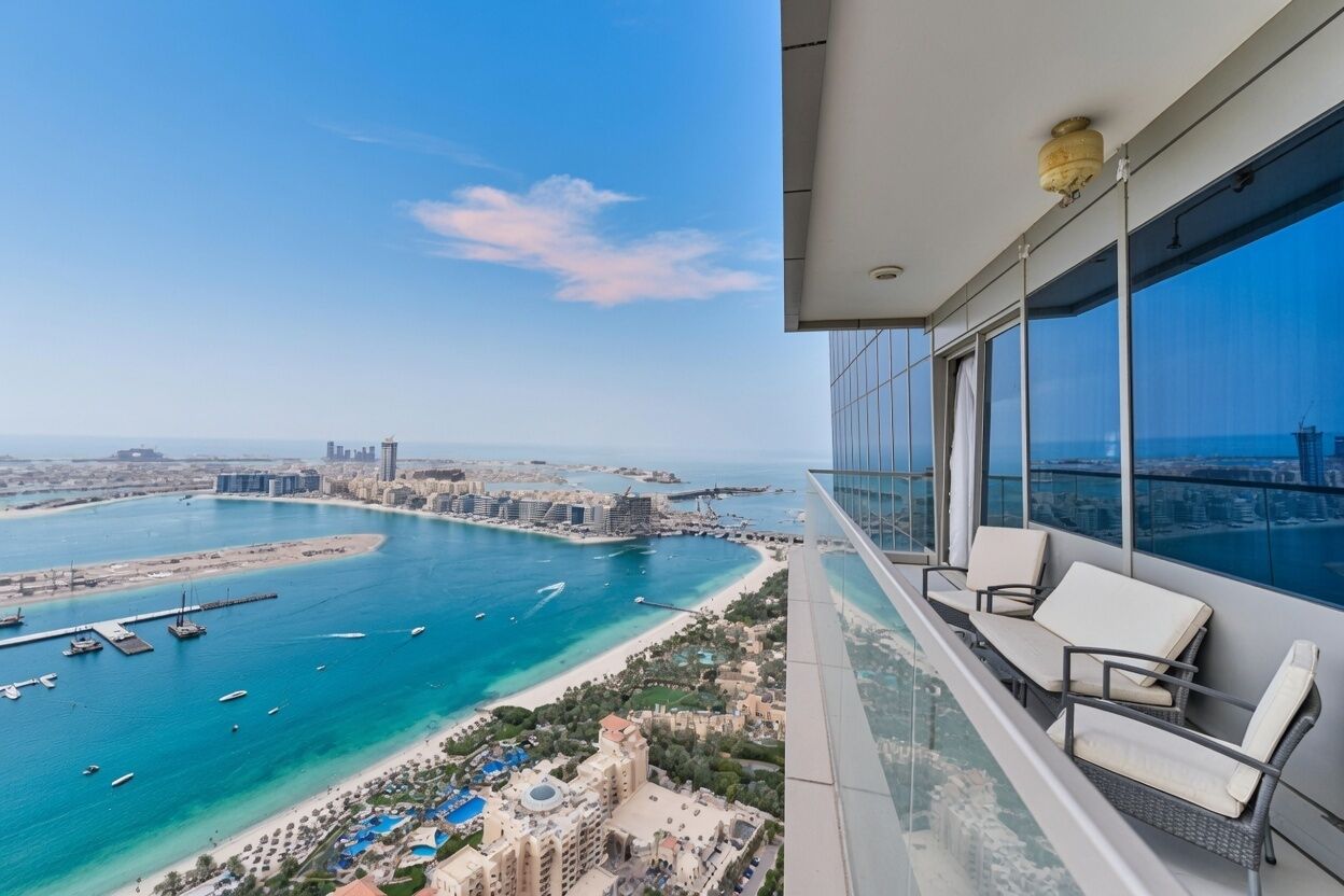 A high-rise balcony with a view of a coastal cityscape, including a marina and beach.