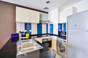 A compact kitchen with a sink, stove, microwave, and washing machine. - Luxury 1BR Ocean Heights, 64th Floor Panoramic Sea and Palm Views with Jacuzzi (Dubai)