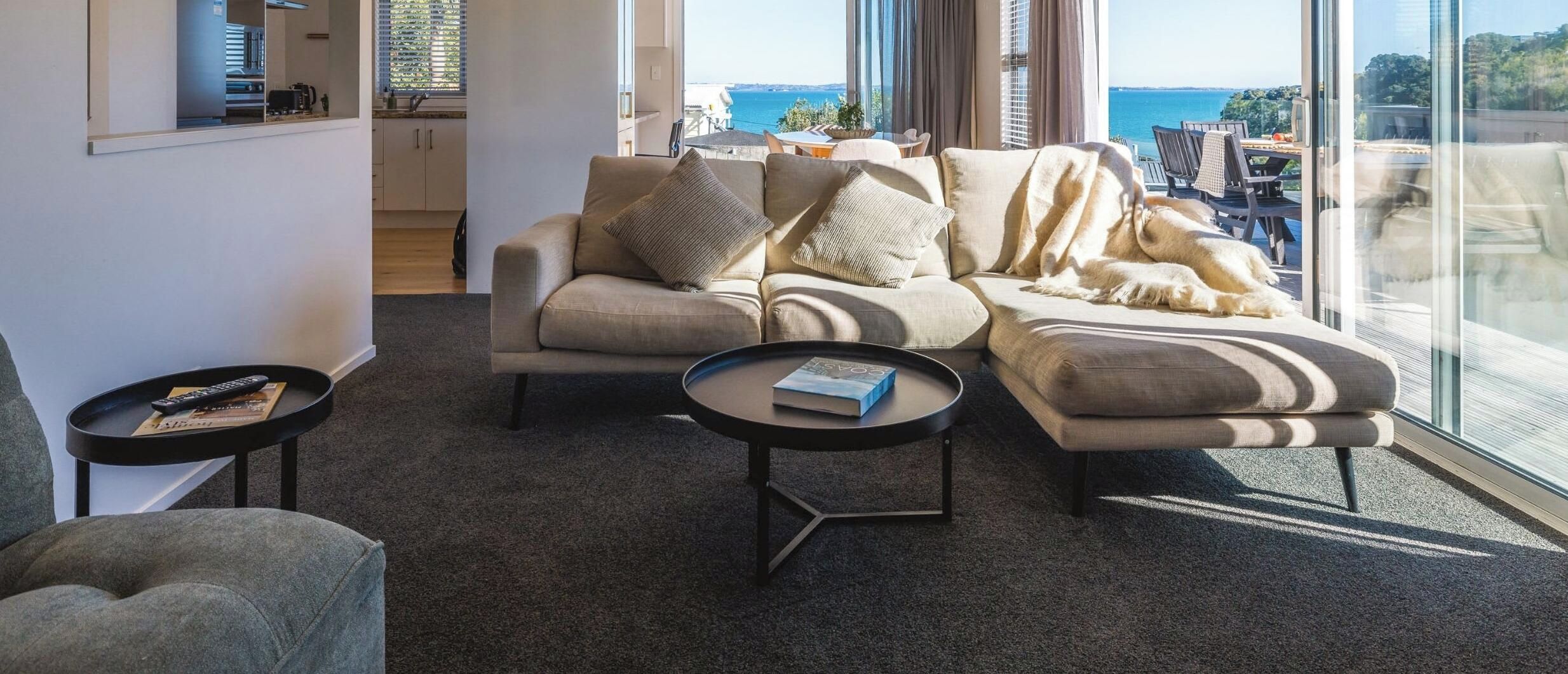 A modern living room with a sofa, a coffee table, and a view of the sea.