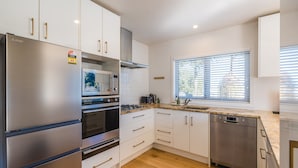 Una cucina moderna con elettrodomestici in acciaio inossidabile, mobili bianchi e una finestra con persiane.