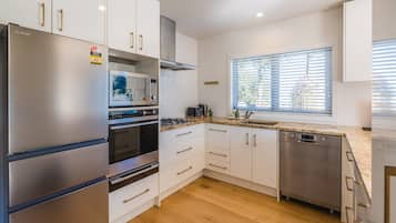 A modern kitchen with stainless steel appliances, white cabinetry, and a window with blinds.