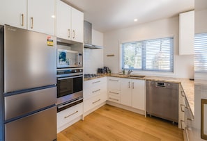 Een moderne keuken met roestvrijstalen apparatuur, witte kastjes en een raam met zonwering.