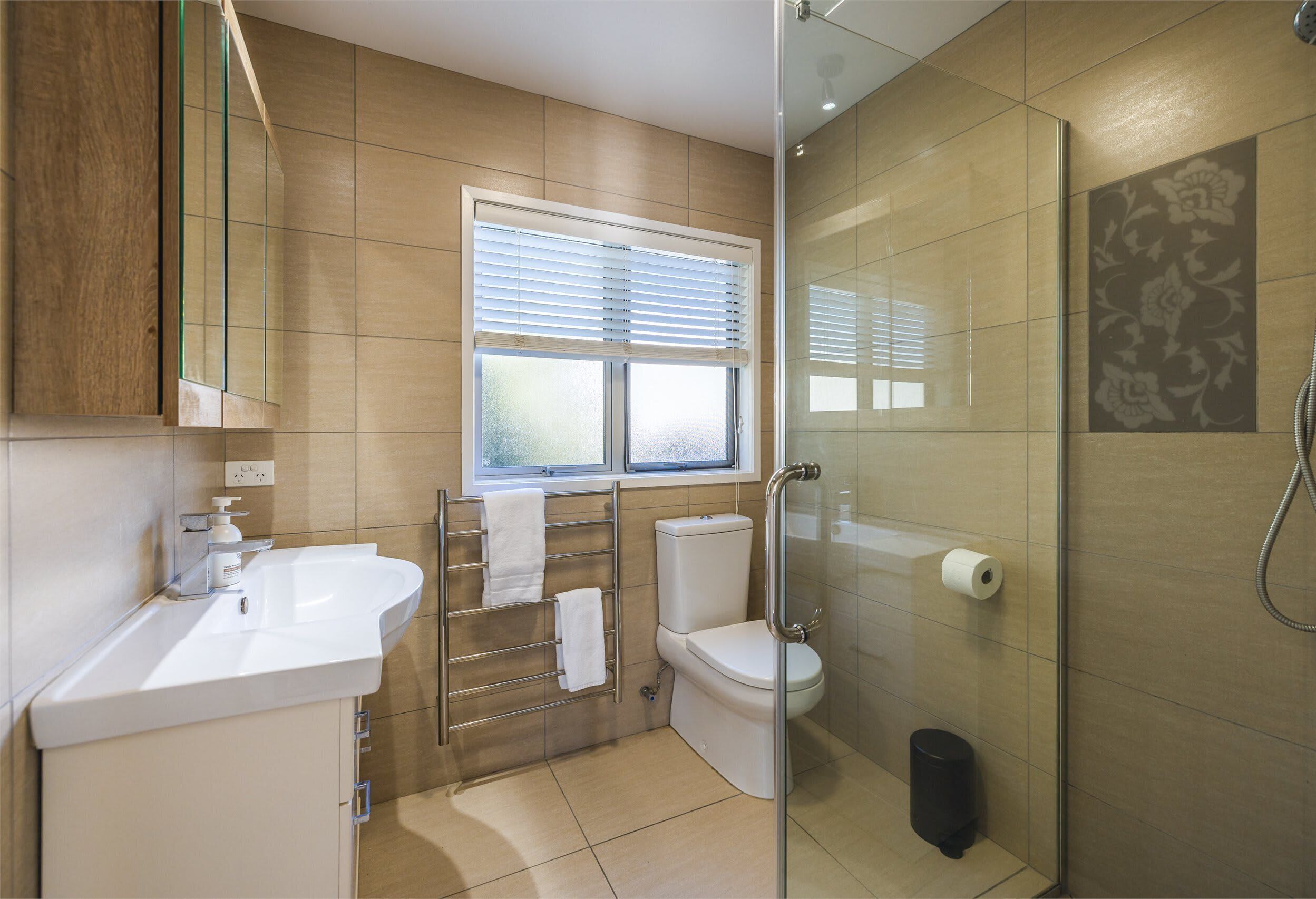 A modern bathroom with a glass shower enclosure, a toilet, a sink, and a window with blinds.