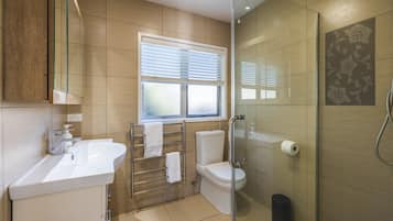 A modern bathroom with a glass shower enclosure, a toilet, a sink, and a window with blinds.