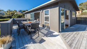 Una casa moderna con una terrazza, un'area pranzo con sedie e un tavolo, e un'ampia porta scorrevole in vetro.