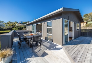 Een modern huis met een terras, een eethoek met stoelen en een tafel, en een grote schuifpui.