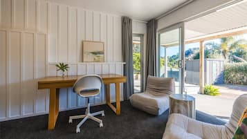 A modern room with a desk, chair, and a sofa. There is a window with curtains, a plant on the desk, and a view of the outdoors.