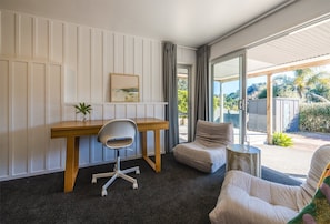 Een moderne kamer met een bureau, stoel en een bank. Er is een raam met gordijnen, een plant op het bureau en uitzicht op het landschap.
