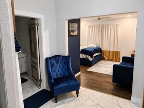 A bedroom with a bed, a blue armchair, a wooden floor, and a white door.