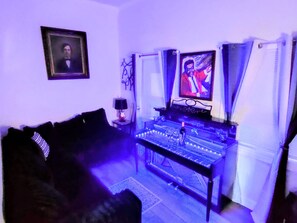 Een kamer met een DJ-installatie, een bank en een lijst aan de muur.
