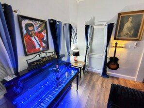 A room with a piano, a guitar, and a framed portrait on the wall. - The Blue Note House: Historic 6-bedroom Marvelous Music-Themed Gulfport Getaway (Gulfport)