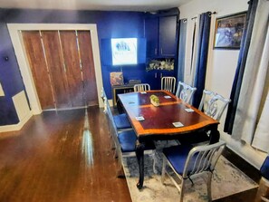 A dining area with a wooden table, blue upholstered chairs, and a television on the wall. - The Blue Note House: Historic 6-bedroom Marvelous Music-Themed Gulfport Getaway (Gulfport)