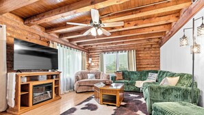 Ein gemütliches Blockhausschlafzimmer mit Holzbalkendecke, einem Flachbildfernseher, einem grünen Sofa und einem rustikalen Kamin.