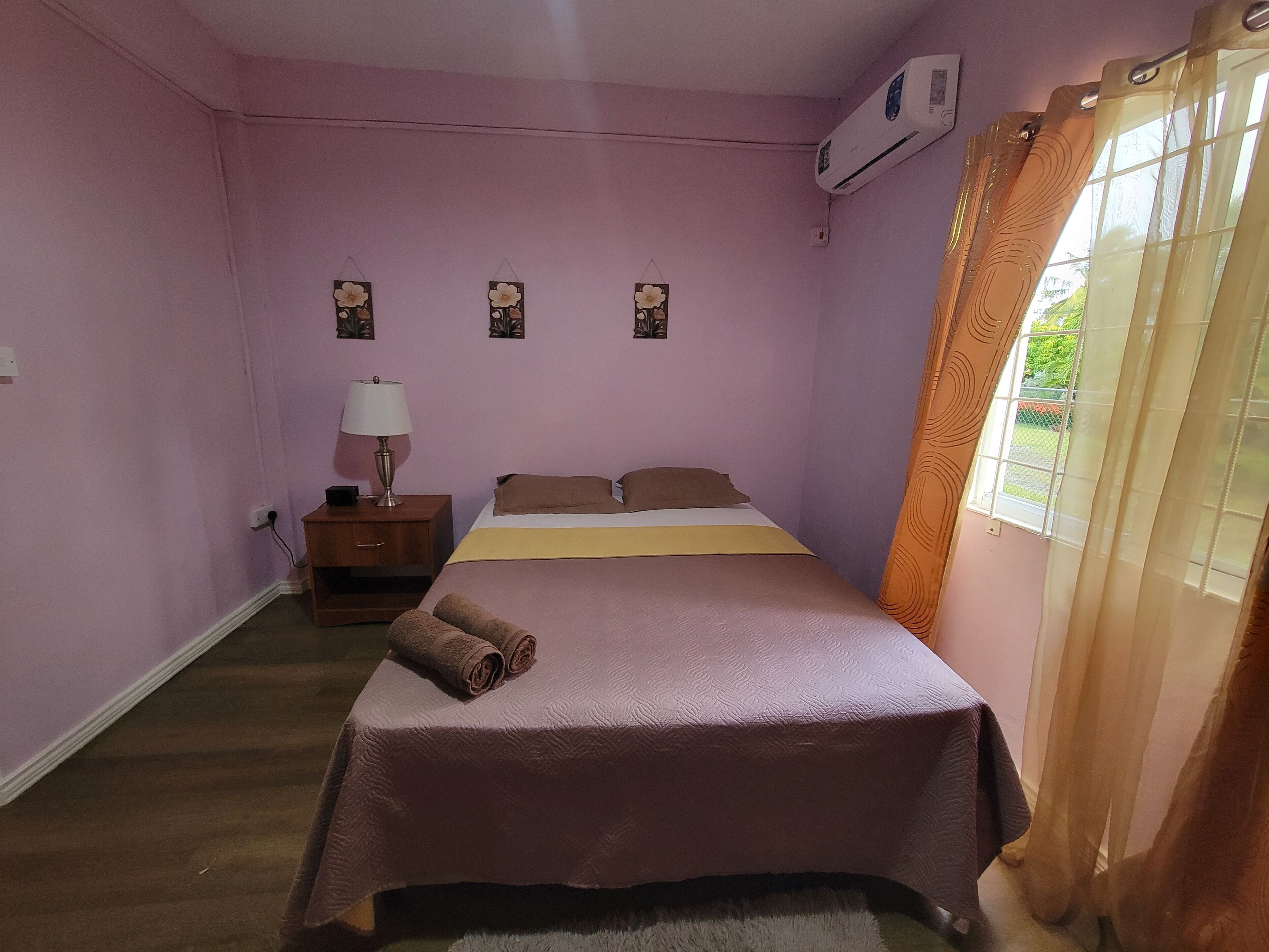 Ein Schlafzimmer mit einem Bett, einem Nachttisch, einer Lampe und einem Fenster mit Vorhängen.