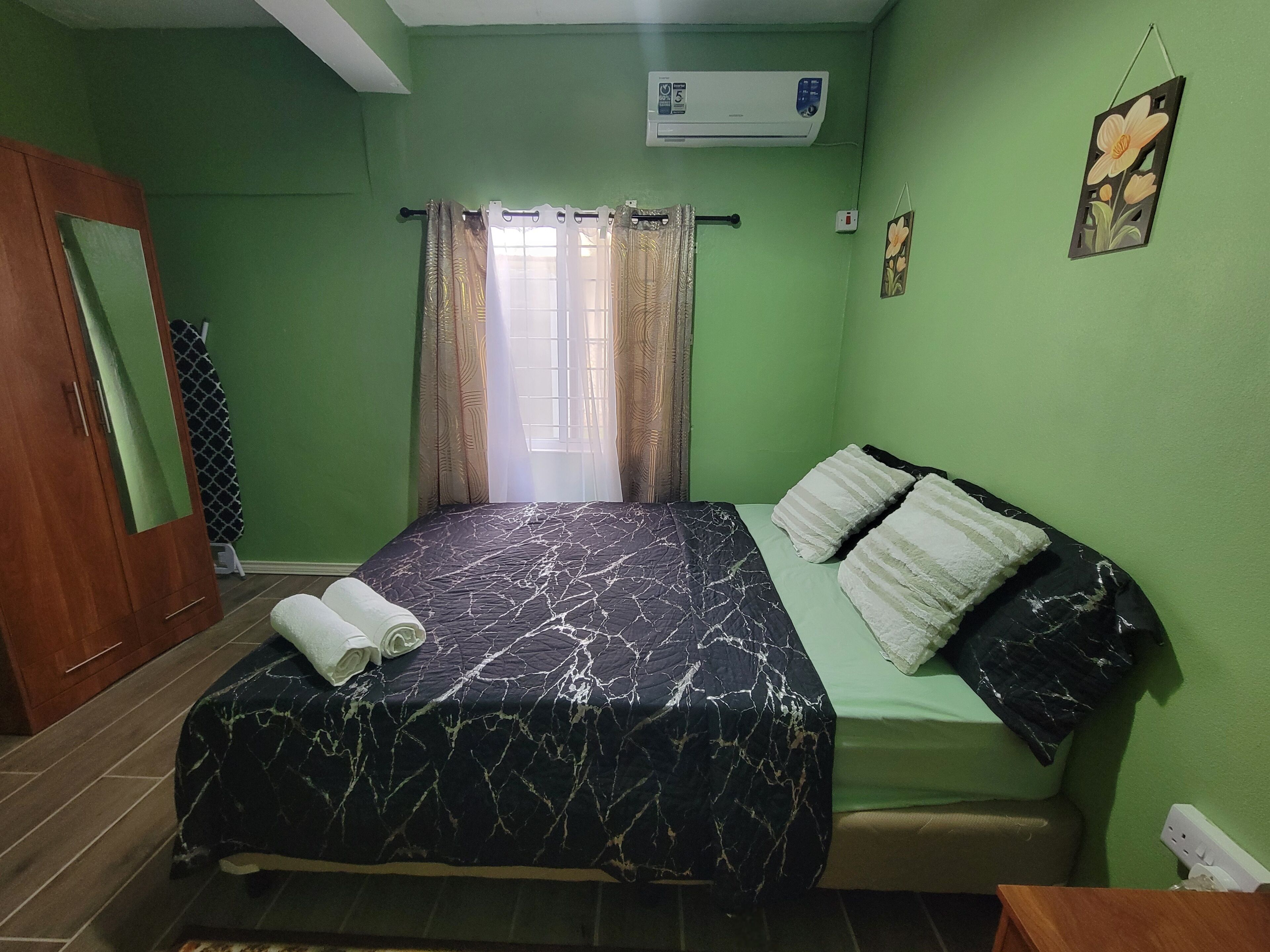 Une chambre comprenant un lit, une armoire, un appareil de climatisation et une fenêtre avec des rideaux.