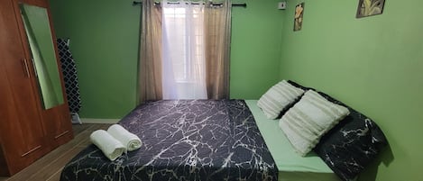 A room with a bed, a wardrobe, an air conditioning unit, and a window with curtains.