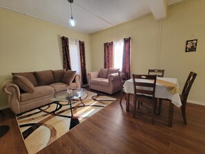 A living room with a sofa, a coffee table, a dining table with chairs, and a patterned rug. - New Listing-Bungalow Verde (Vieux Fort)