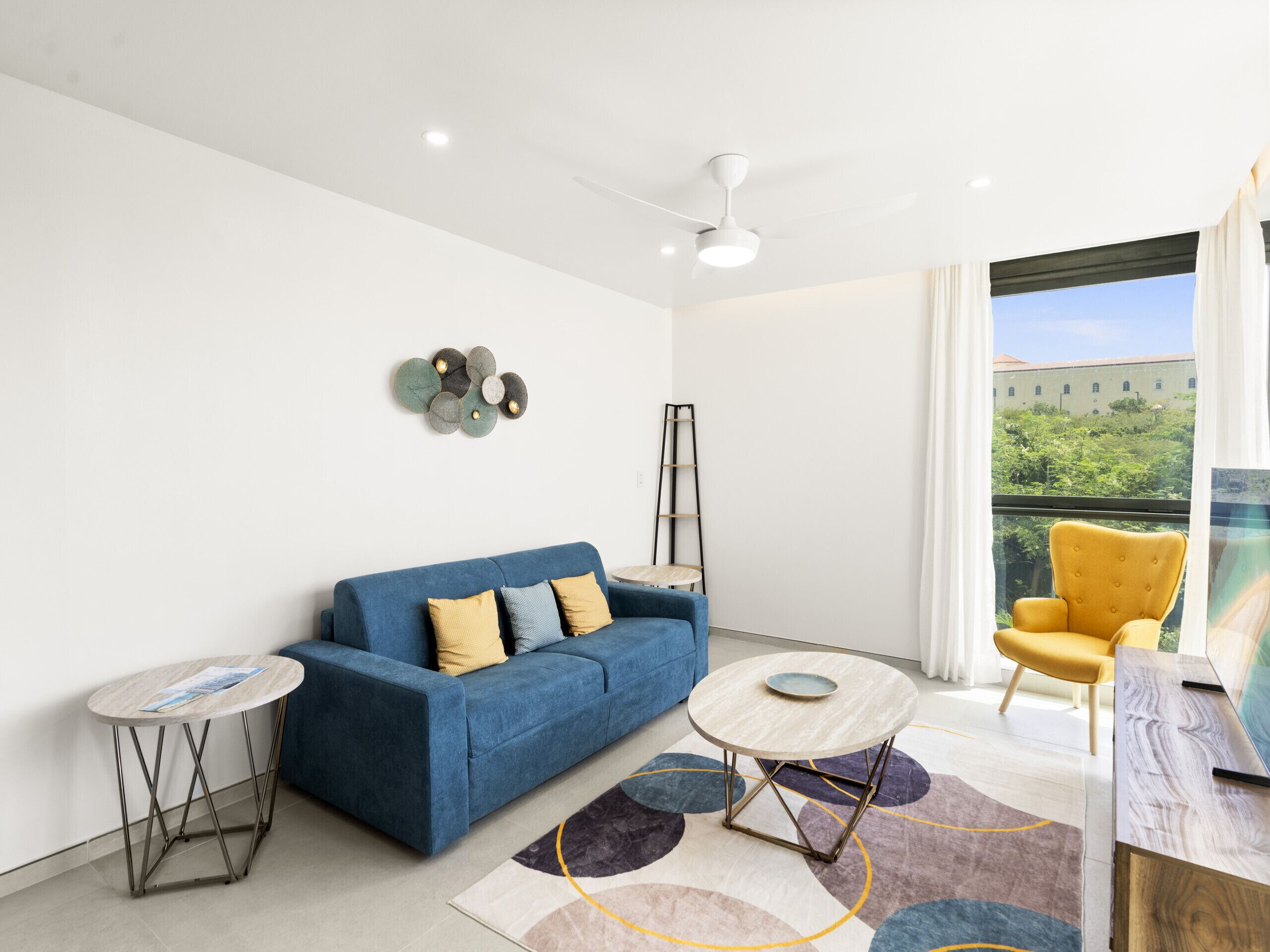 A modern living room with a blue sofa, a yellow armchair, a round coffee table, and a small side table.