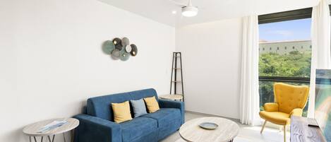 A modern living room with a blue sofa, a yellow armchair, a round coffee table, and a small side table.