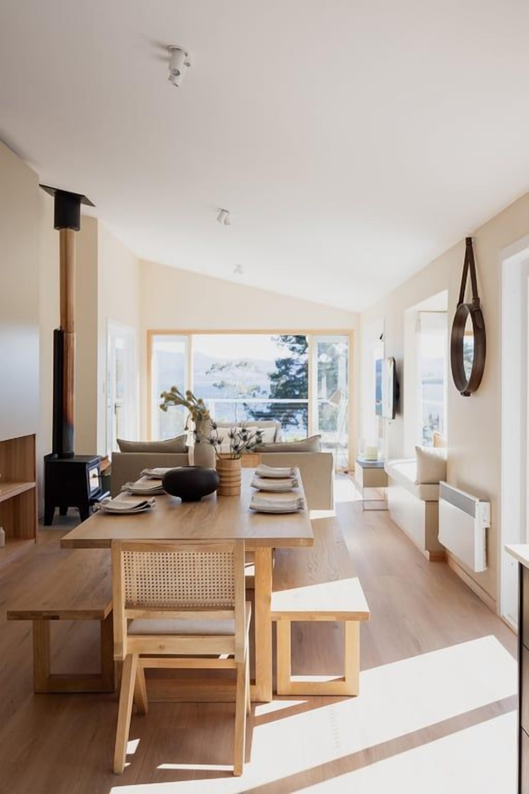 A modern interior with a dining area, a sofa, and a view through large windows.