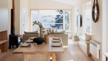 A modern interior with a dining area, a sofa, and a view through large windows.