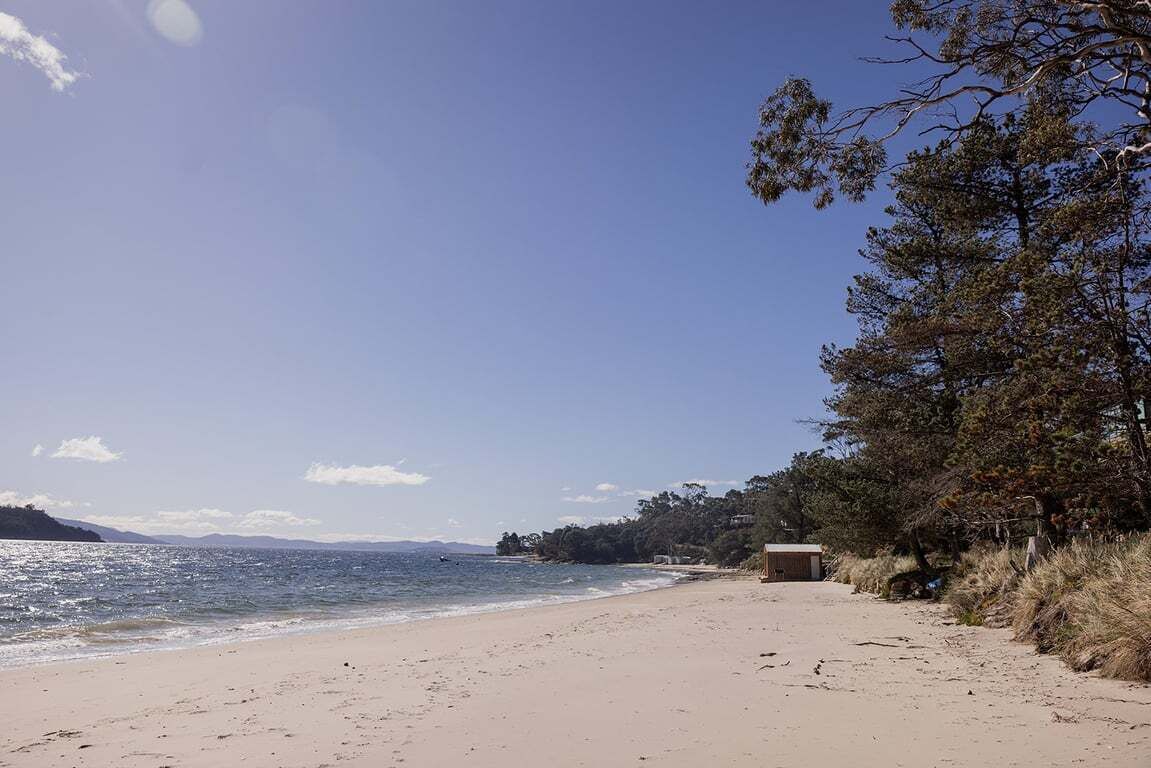 Une plage avec un ciel dégagé, un rivage sablonneux et un petit bâtiment situé près de l’eau.