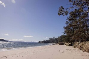 A beach with a clear sky, a sandy shore, and a small building near the water.