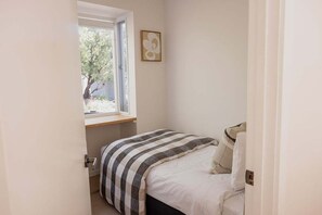 A small bedroom with a single bed, a window, and a door.