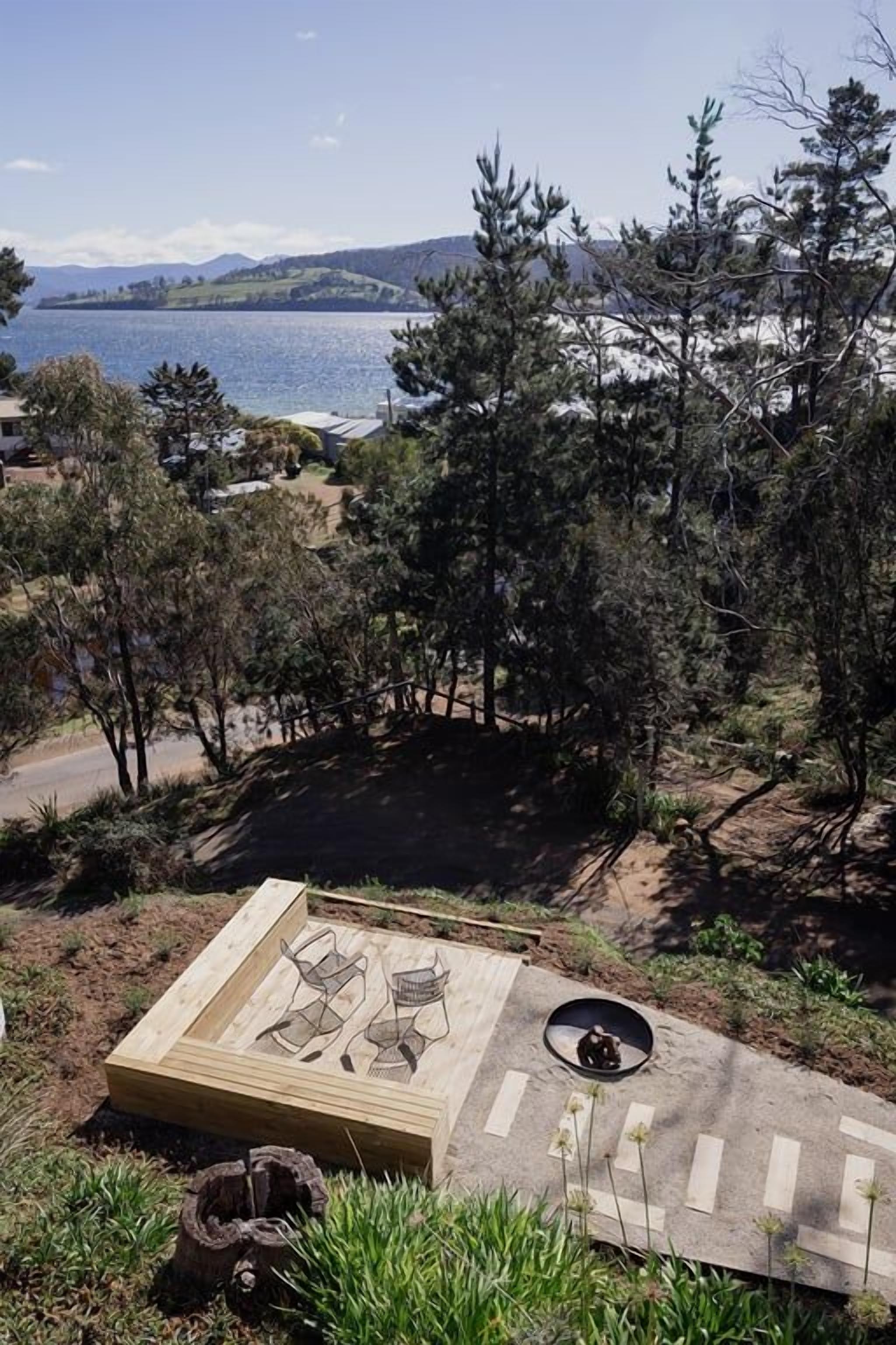 A wooden deck with outdoor furniture, a fire pit, and a view of a lake and hills.