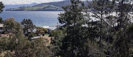 A wooden deck with outdoor furniture, a fire pit, and a view of a lake and hills.