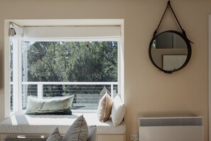 A room with a window seat, a round mirror, and a radiator.