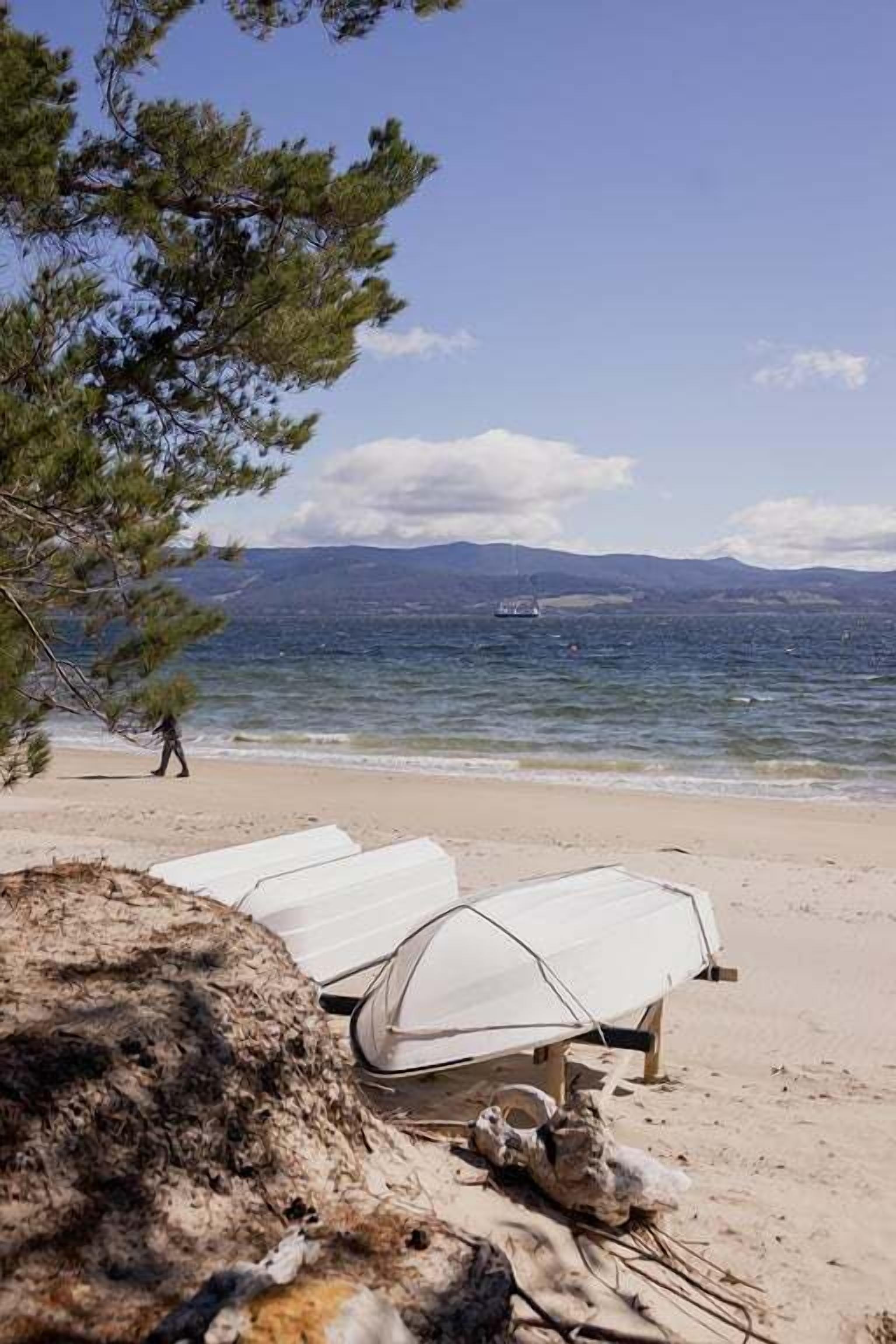 Ein Strand mit weißen Zelten und freiem Blick auf das Meer und ferne Berge.