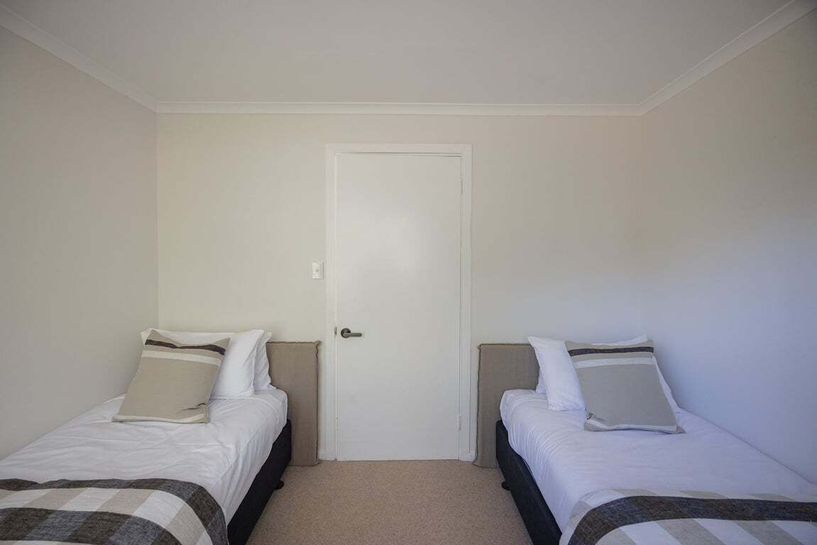A room with two single beds, a white door, and a carpeted floor.