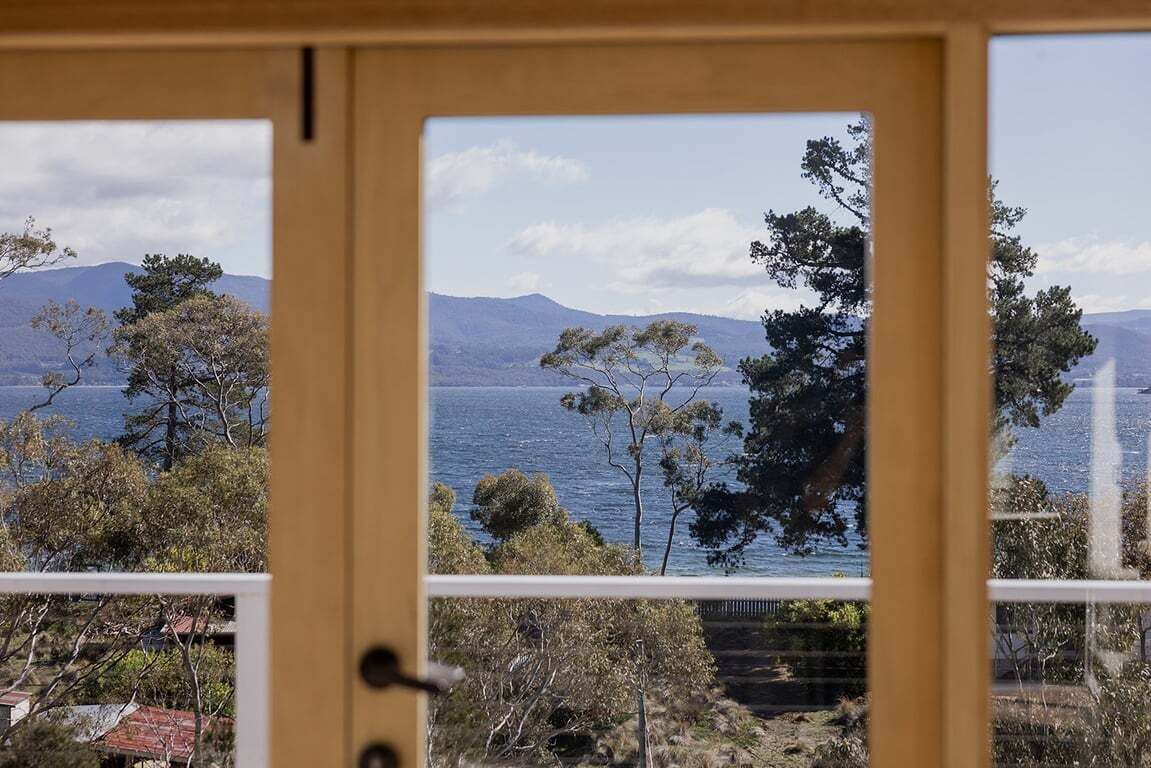 A view through a window with a door, featuring a landscape with trees and a body of water.