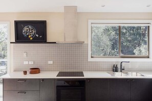 A modern kitchen with a large window, a built-in oven, and a backsplash. - Graceys Beach House Dennes Point (Kingborough)