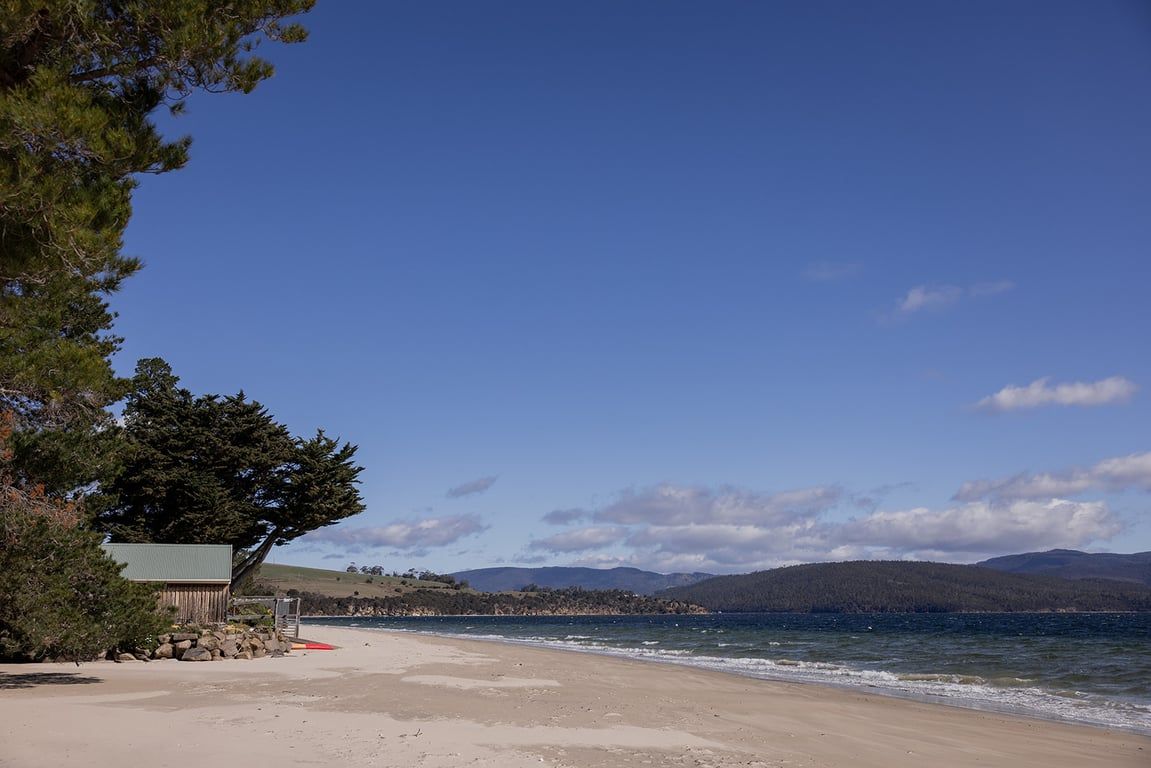 A beach with a small building, clear skies, and distant hills.