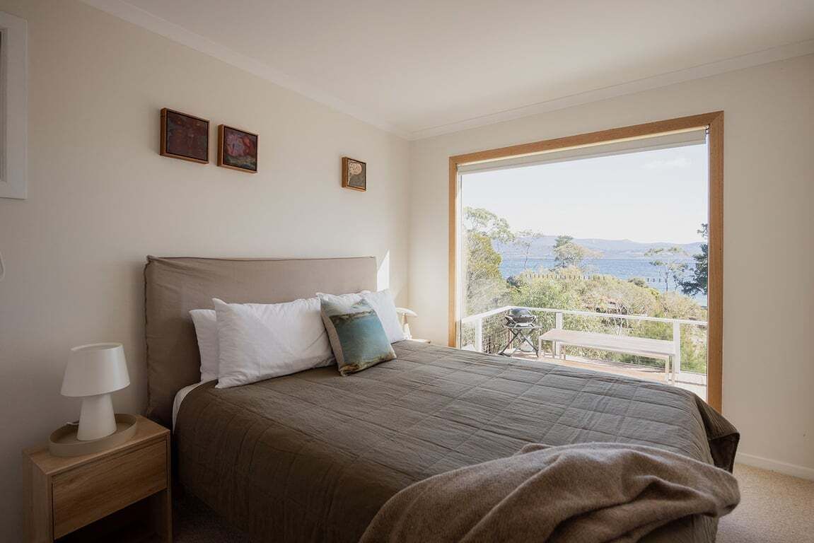 Une chambre avec un grand lit, une table de chevet, une lampe et une vue sur l’extérieur grâce à une porte coulissante.