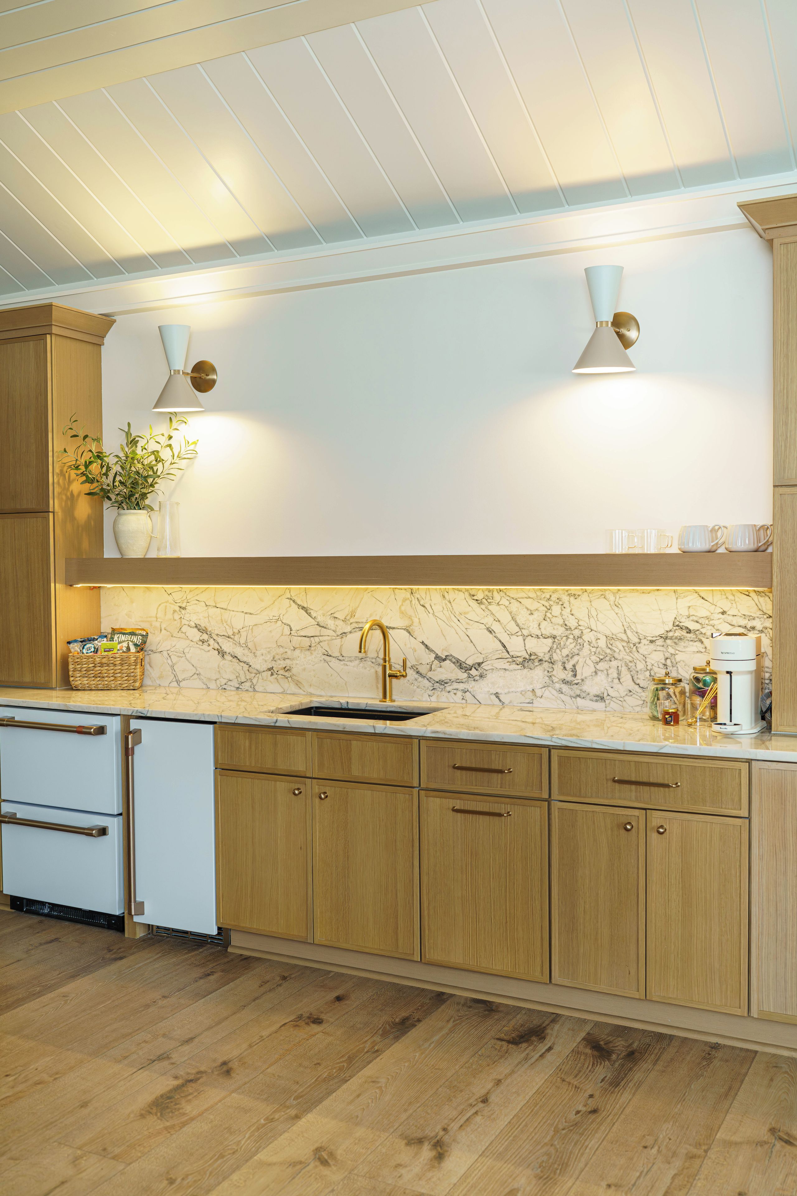 A modern kitchen with wooden cabinets, a marble countertop, a sink, and a coffee maker.