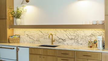 A modern kitchen with wooden cabinets, a marble countertop, a sink, and a coffee maker.