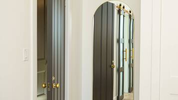 A hallway with a wooden floor, a white door, and a mirror reflecting a door with a golden handle.