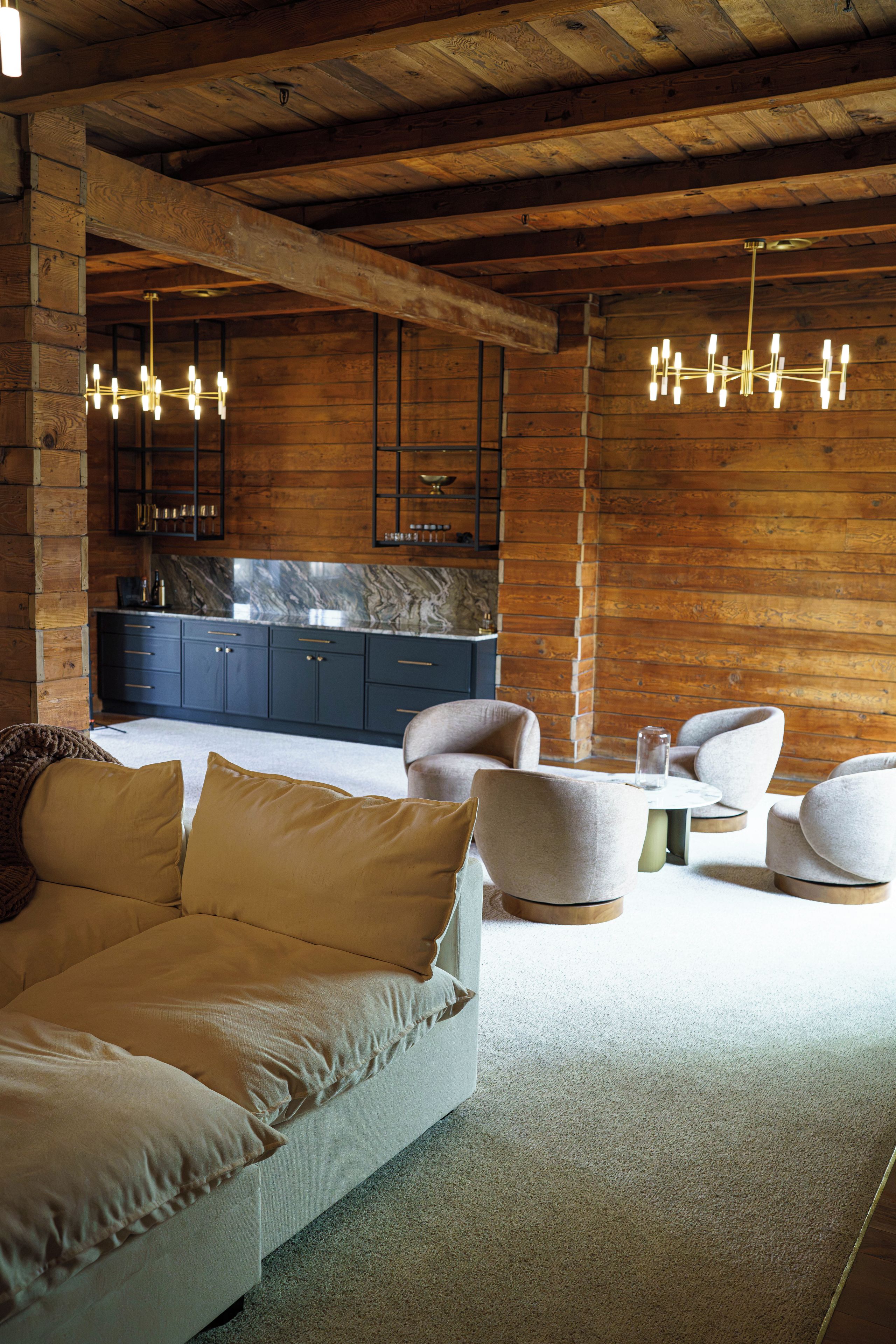 A modern interior with a sofa, chairs, a kitchen area, and wooden beams.