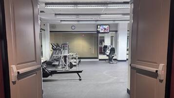 Ingresso di un hotel con reception, uno schermo digitale e attrezzature per esercizi in sottofondo.