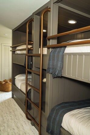 A bunk bed room with a ladder, a bed with a blanket, and a small seating area.