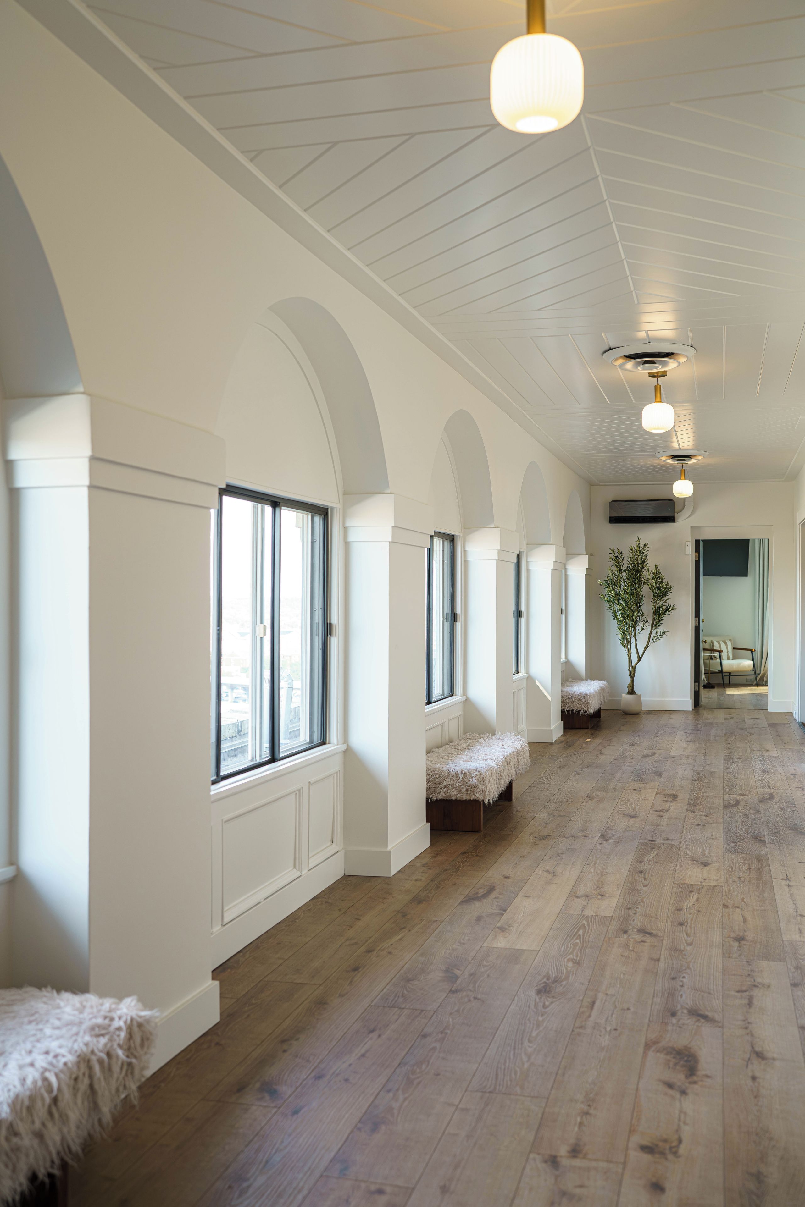 A spacious hallway with white walls, wooden flooring, and multiple windows.