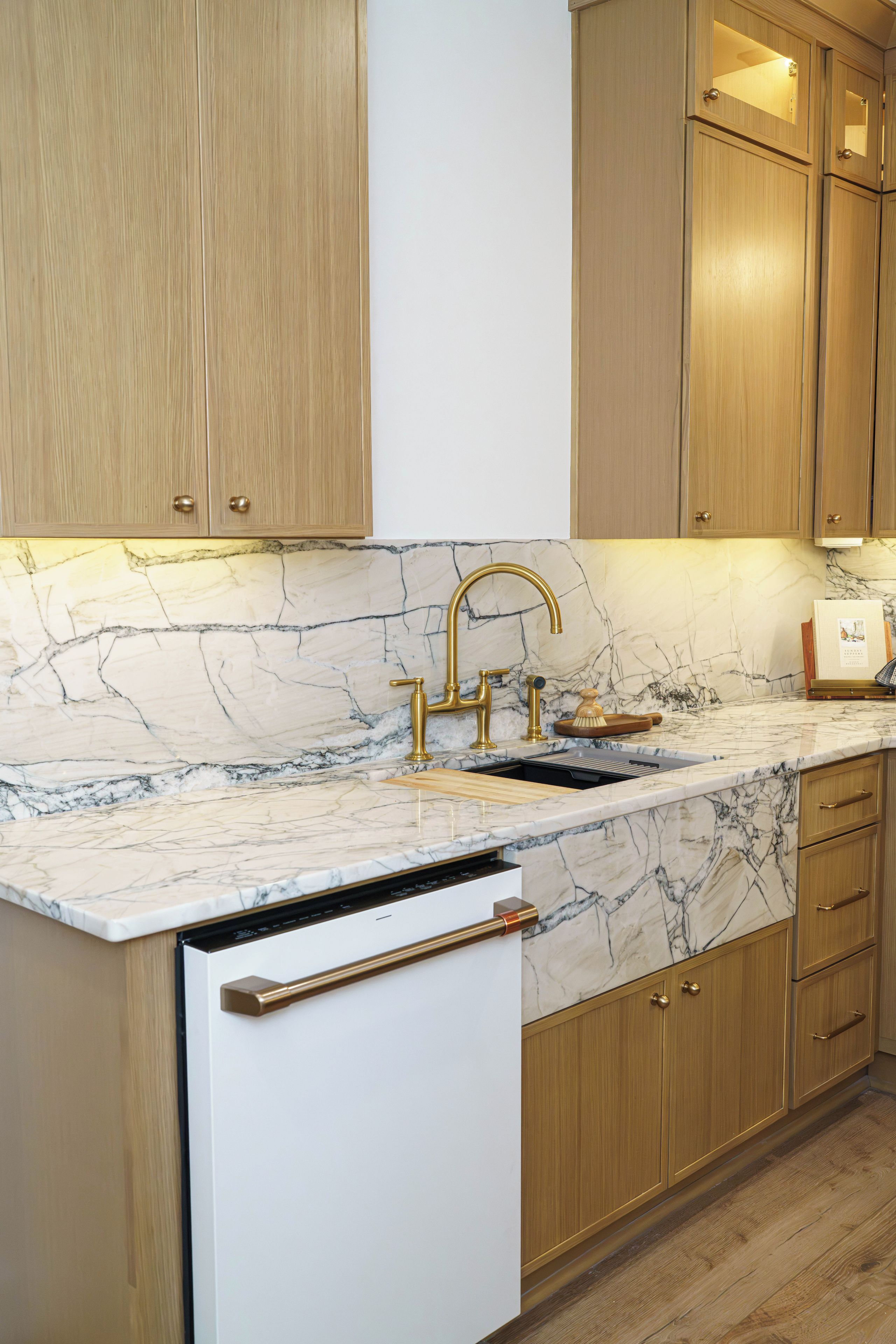 A kitchen with a marble countertop, gold faucets, and wooden cabinets.