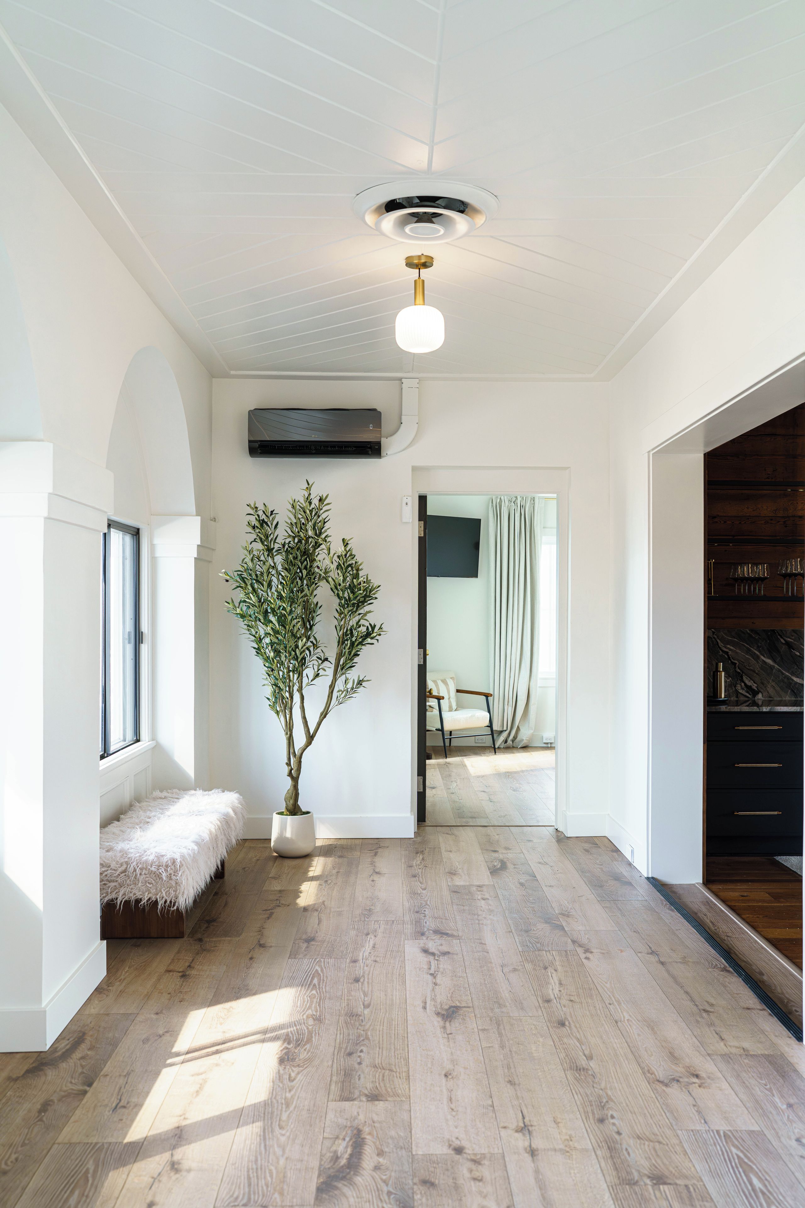 A spacious hallway with a wooden floor, a white bench, a potted plant, and a ceiling fan.