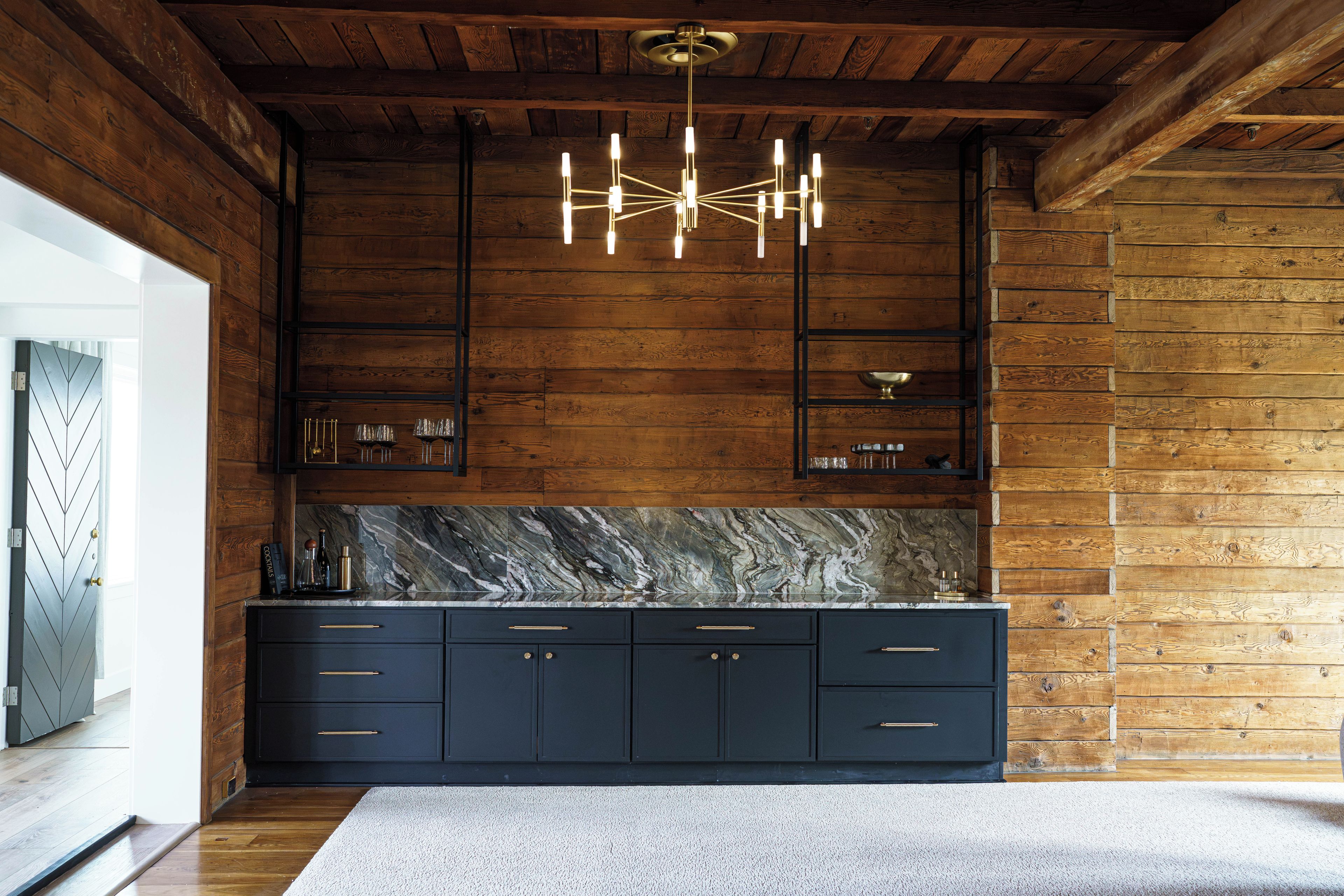 A modern kitchen with dark cabinetry, a marble countertop, and a unique chandelier.