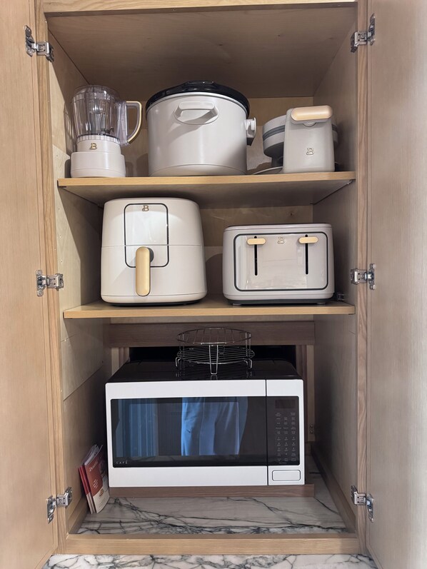 A kitchen cabinet with a microwave, toaster, blender, and slow cooker.