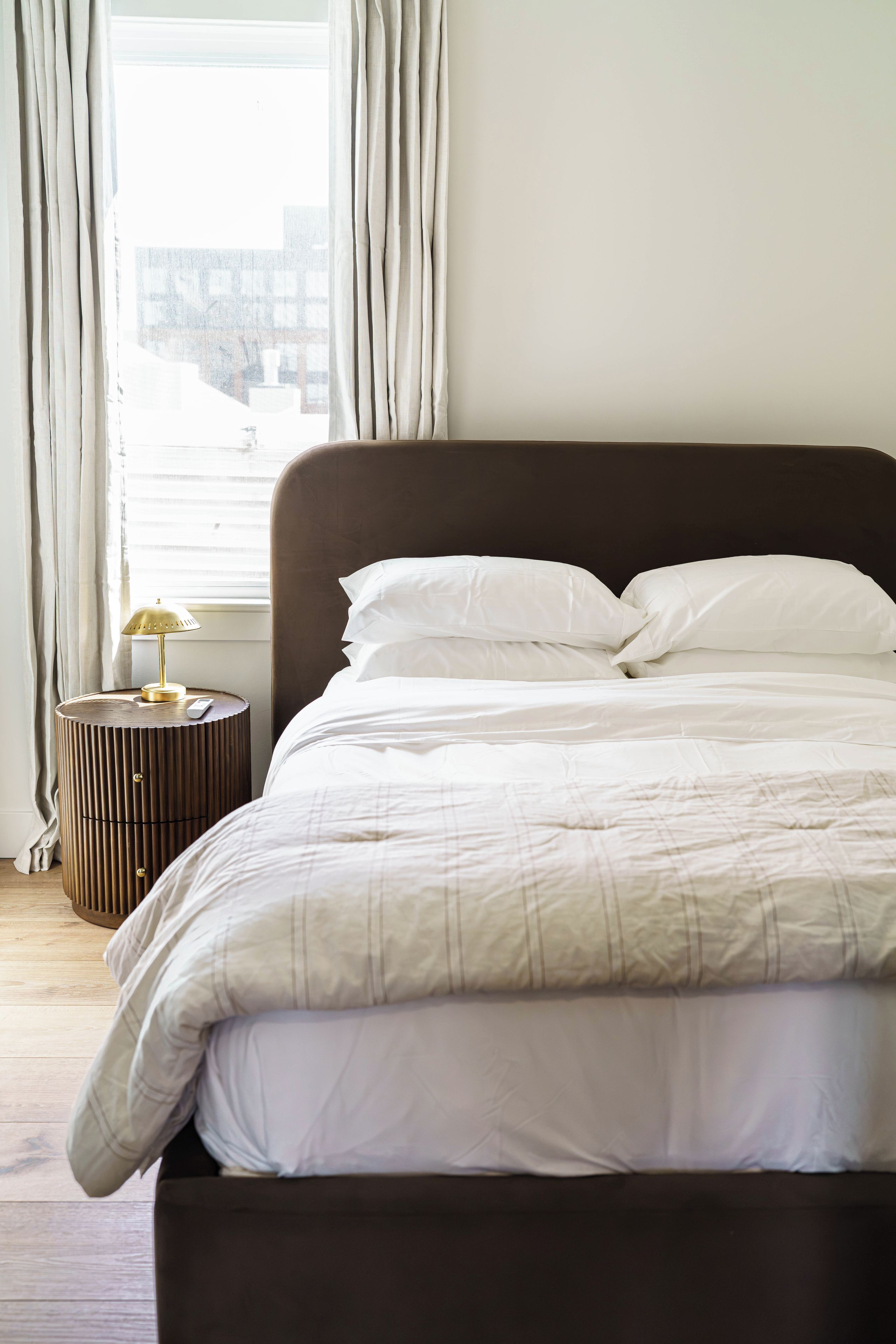 A bed with white bedding, a round bedside table with a lamp, and a window with curtains.