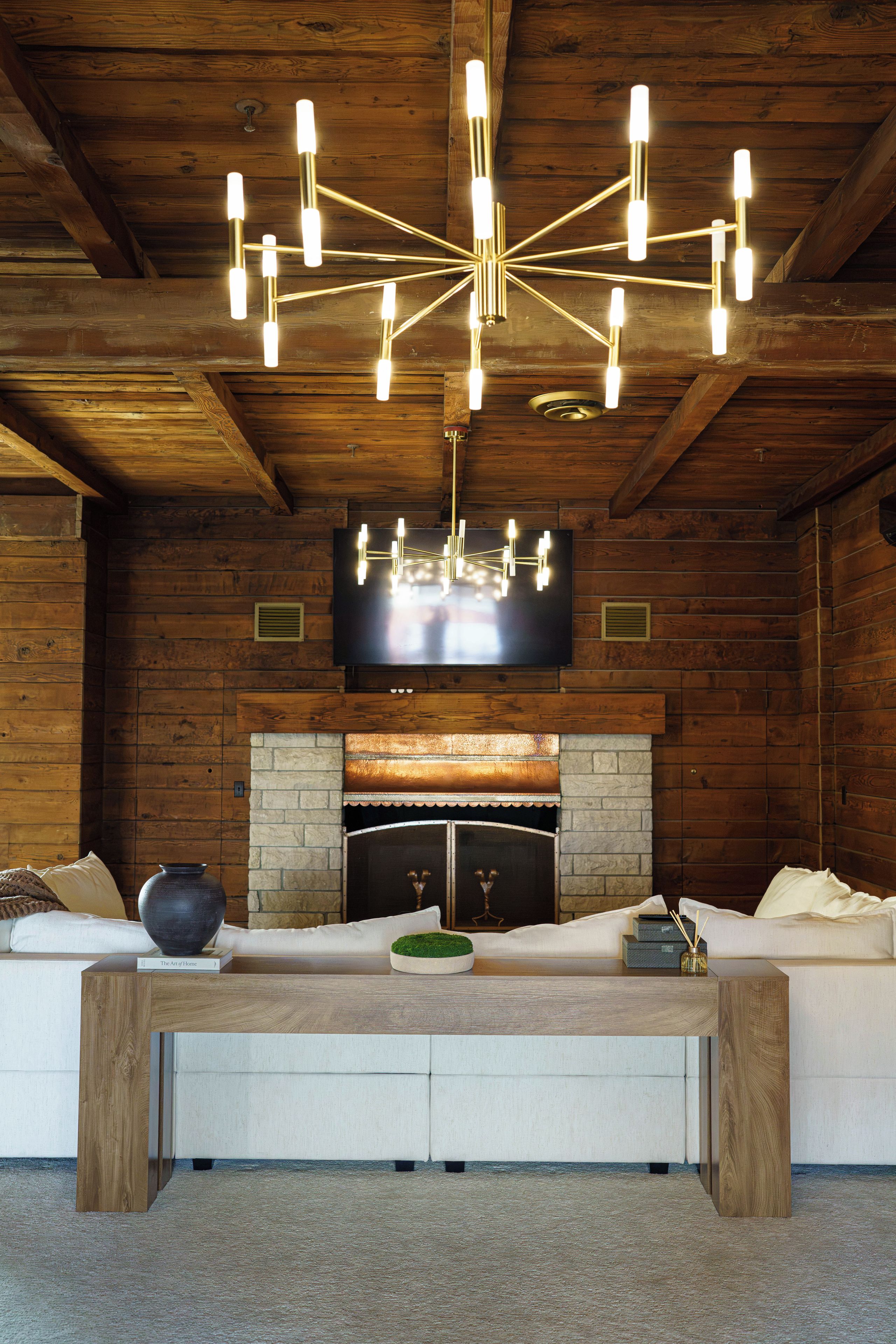 A cozy interior with a wooden ceiling, a fireplace, a sofa, and a modern chandelier.